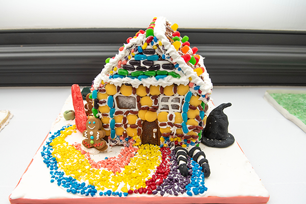 A heavily decorated gingerbread house adorned with many different types of candies. A yellow brick road leading to the door highlights the witch's legs sticking out from underneath the house's foundation.