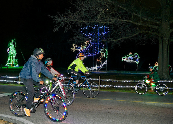Group of three on bikes passing whale made of holiday lights.