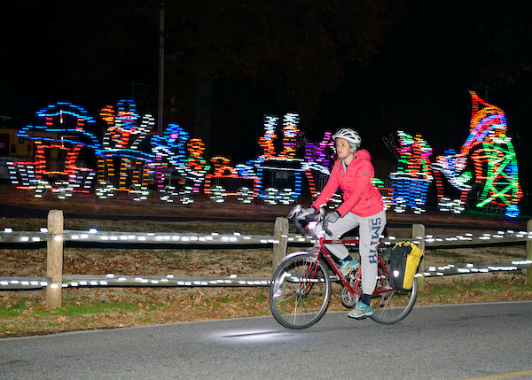 Person on bike in red sweater passing train made of holiday lights