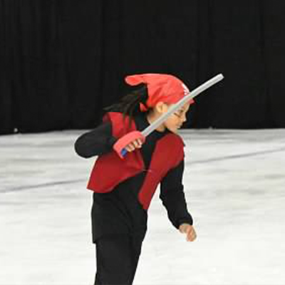 A kid dressed up as a red pirate with a foam sword skating across the ice