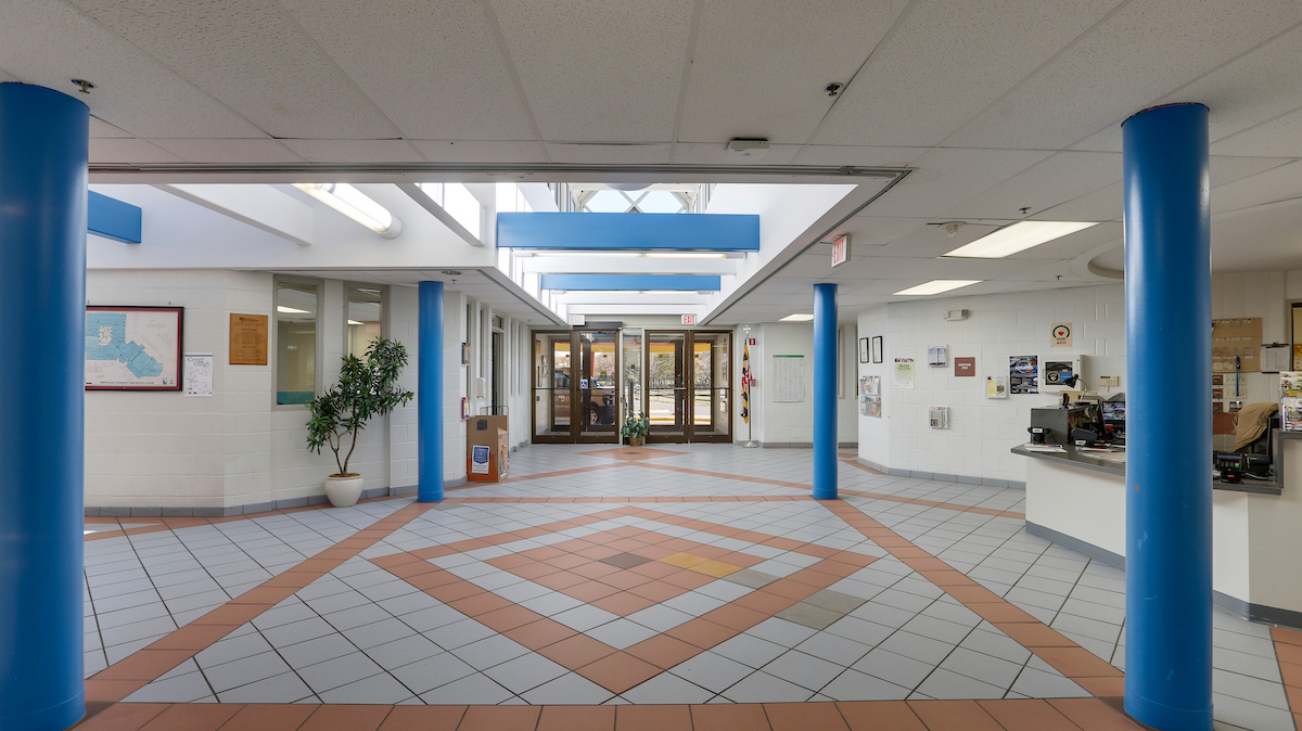 A large lobby space with a tiled floor, blue columns, a reception desk, and skylights.