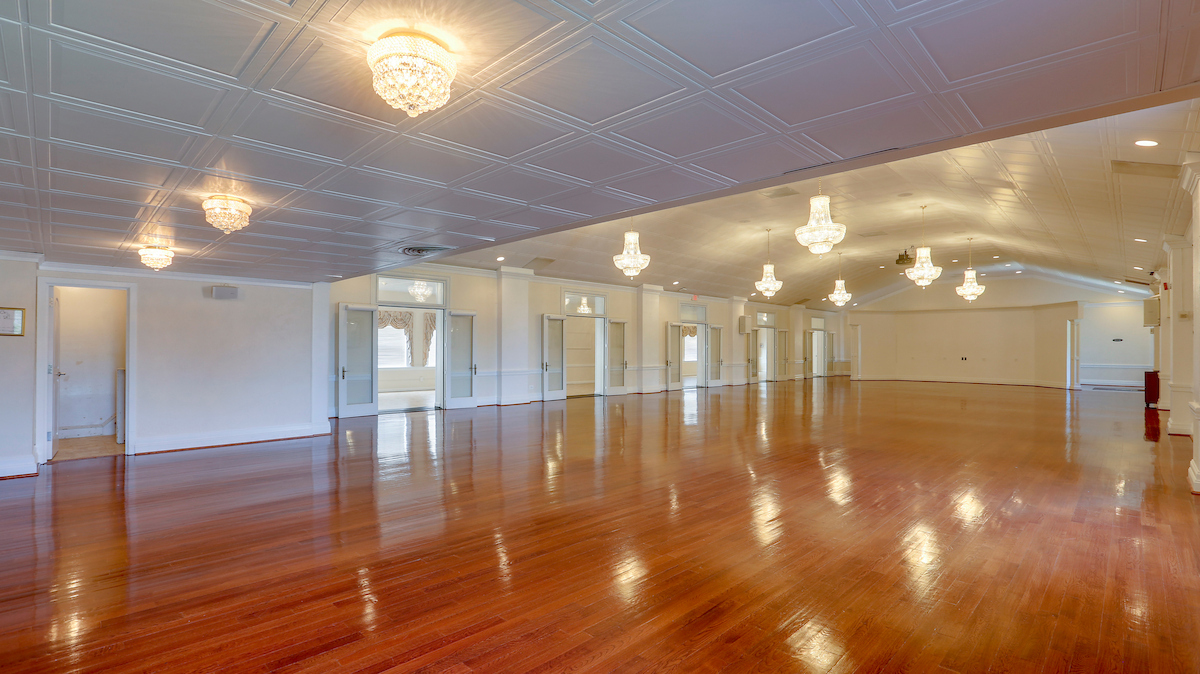 A large ballroom with hardwood floors, crystal chandeliers and light fixtures, and rows of double doors along the far side leading into an adjacent room.