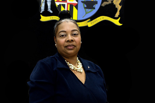 A woman in a dark blue shirt against a black background with a crest above her.
