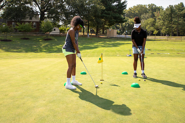 Two teens practice putting on a sunny golf course.