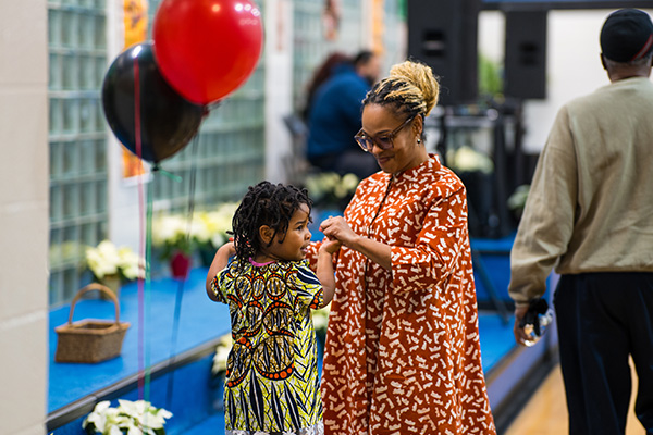 A mother and toddler dance together in a gymnasium decorated with balloons and flowers.