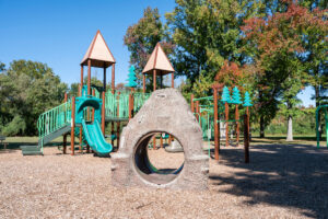 A playground with a large play structure featuring towers, platforms, slides, monkey bars, stairs, fake boulders, and swings.