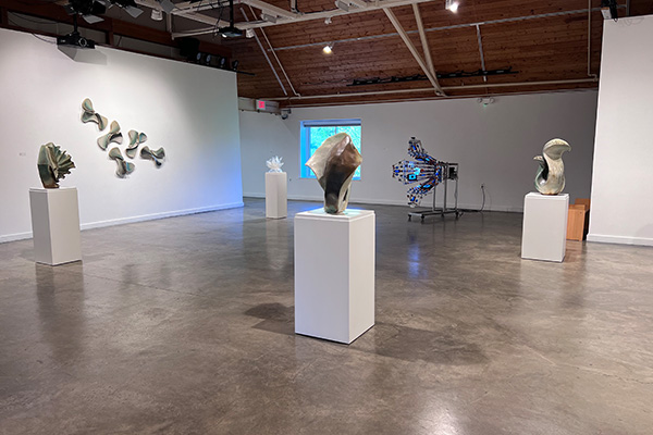 Sculptures on display in an art gallery with white walls and a peaked, wooden ceiling.