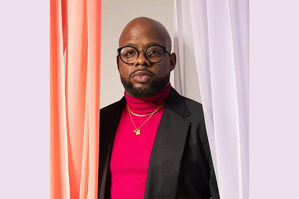 Headshot of a man in glasses wearing a black jacket and a red turtleneck.