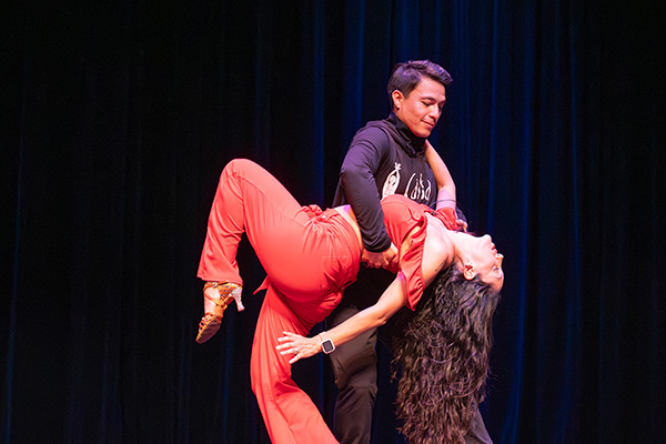 A woman in red dances on a stage with a man in a black shirt.