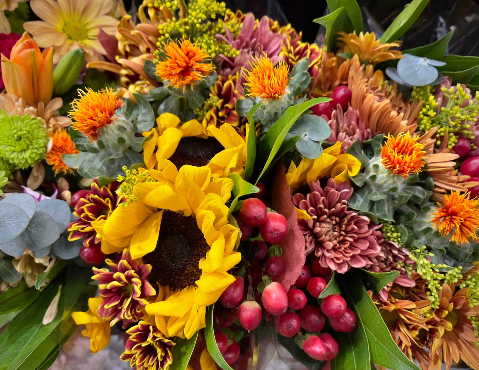An overhead view of a vibrant autumn flower arrangement featuring sunflowers, chrysanthemums, and red berries.